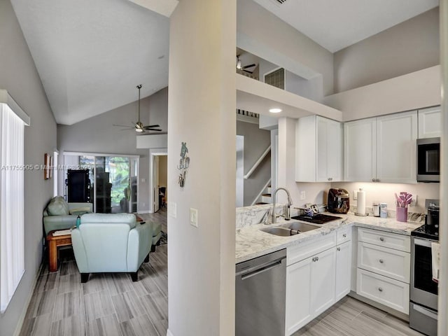 kitchen featuring stainless steel appliances, open floor plan, white cabinetry, a sink, and light stone countertops