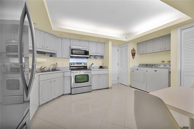 kitchen featuring stainless steel appliances, a sink, light countertops, washer and clothes dryer, and a raised ceiling