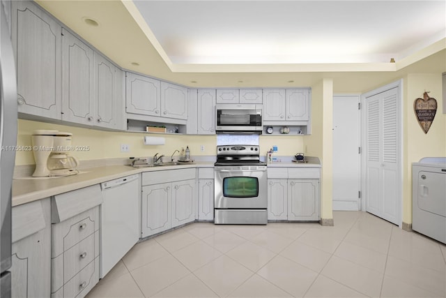 kitchen featuring light tile patterned floors, stainless steel appliances, a sink, light countertops, and washer / clothes dryer