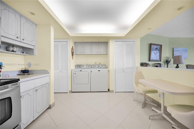 kitchen featuring a tray ceiling, light tile patterned floors, light countertops, electric range, and separate washer and dryer