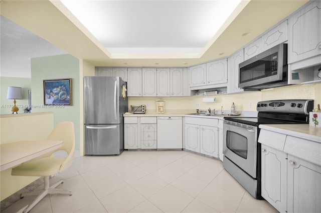 kitchen featuring light tile patterned floors, a raised ceiling, stainless steel appliances, light countertops, and a sink