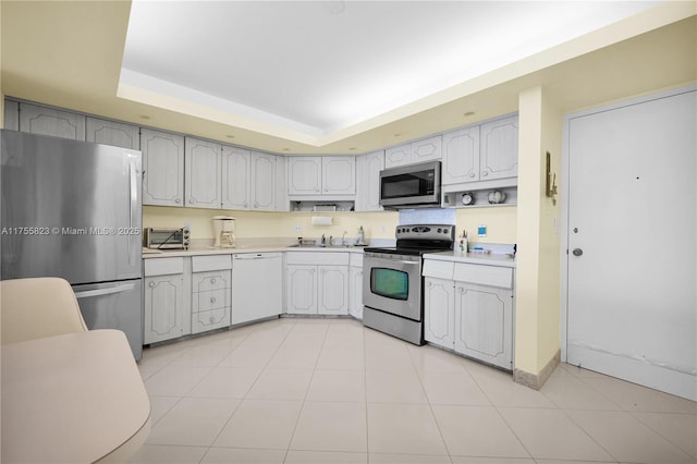 kitchen with light tile patterned floors, a raised ceiling, appliances with stainless steel finishes, light countertops, and a sink