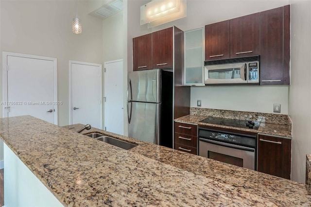 kitchen featuring light stone counters, appliances with stainless steel finishes, glass insert cabinets, a sink, and dark brown cabinets