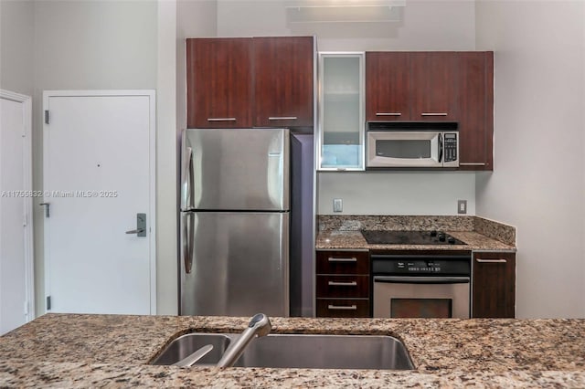 kitchen with appliances with stainless steel finishes, glass insert cabinets, a sink, and light stone countertops