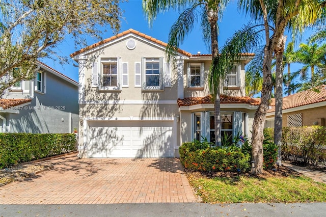 mediterranean / spanish-style house featuring a tiled roof, decorative driveway, an attached garage, and stucco siding