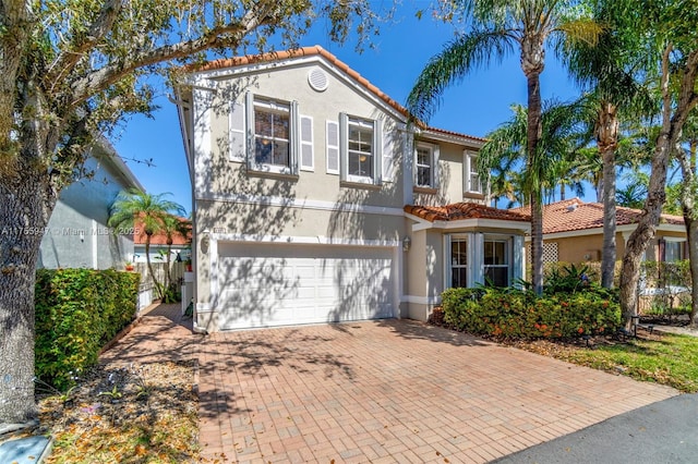 mediterranean / spanish-style house featuring a garage, decorative driveway, a tiled roof, and stucco siding