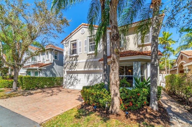 mediterranean / spanish-style home with a garage, decorative driveway, a tile roof, and stucco siding