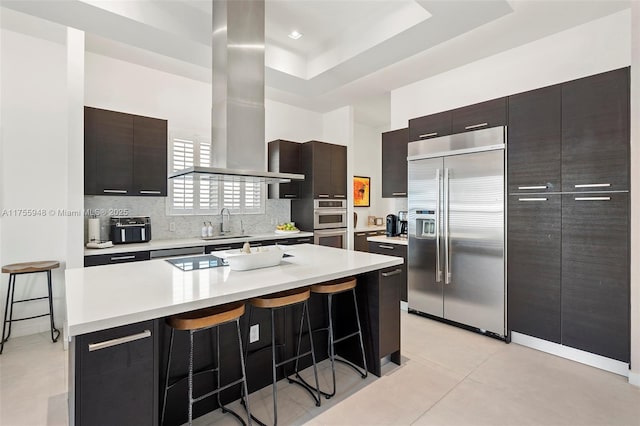 kitchen with exhaust hood, built in refrigerator, modern cabinets, and a breakfast bar area