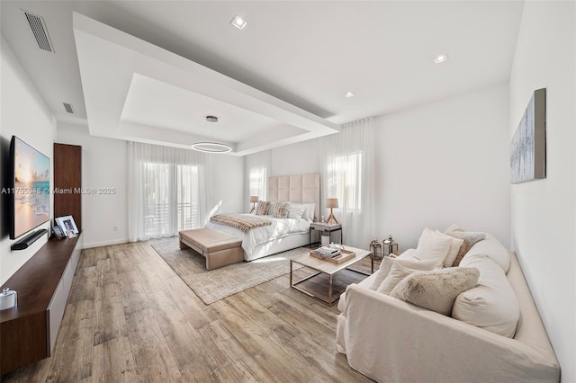 living area featuring plenty of natural light, visible vents, a tray ceiling, and wood finished floors