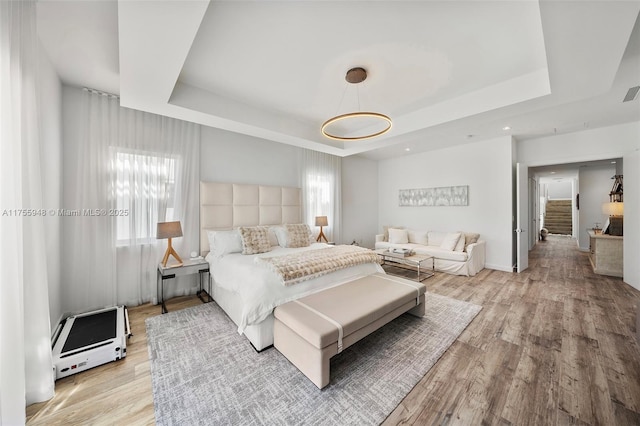 bedroom with light wood-type flooring, a raised ceiling, and visible vents