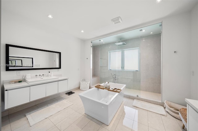 full bath with tile patterned flooring, walk in shower, vanity, a freestanding tub, and recessed lighting