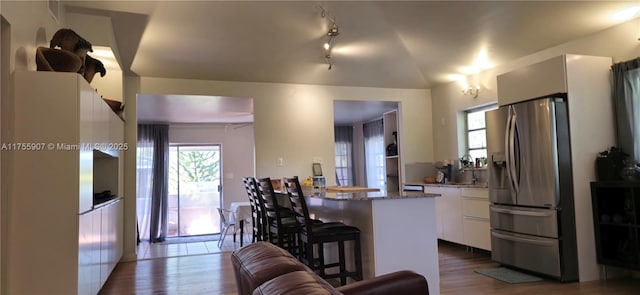 kitchen with a kitchen breakfast bar, stainless steel refrigerator with ice dispenser, wood finished floors, and white cabinets