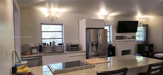 kitchen featuring a fireplace, appliances with stainless steel finishes, white cabinets, a sink, and light stone countertops