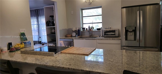 kitchen featuring a toaster, a sink, white cabinetry, appliances with stainless steel finishes, and light stone countertops