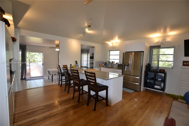 kitchen with a kitchen breakfast bar, a peninsula, stainless steel fridge with ice dispenser, and wood finished floors