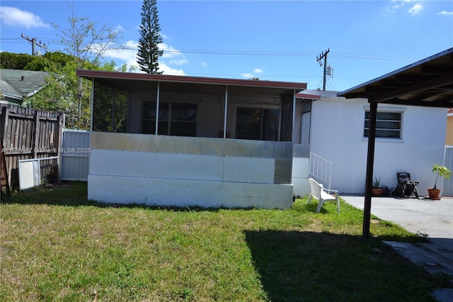 rear view of property featuring a sunroom, a lawn, and fence