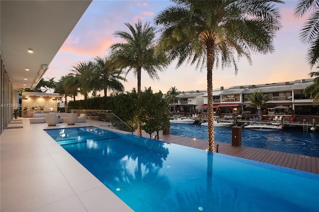 pool at dusk featuring a dock, a patio area, outdoor lounge area, and an infinity pool