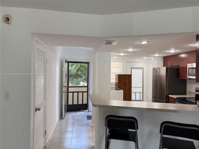 kitchen featuring light tile patterned floors, a breakfast bar area, stainless steel appliances, a peninsula, and visible vents