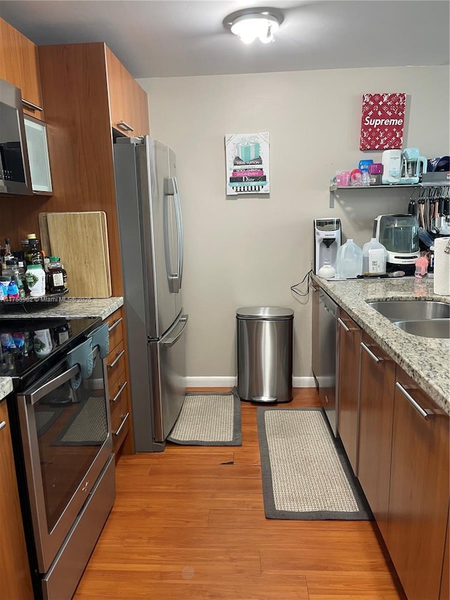 kitchen with light stone counters, light wood-style flooring, a sink, appliances with stainless steel finishes, and brown cabinetry