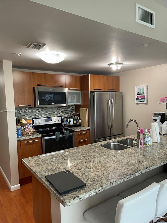 kitchen featuring visible vents, brown cabinetry, a breakfast bar, stainless steel appliances, and a sink