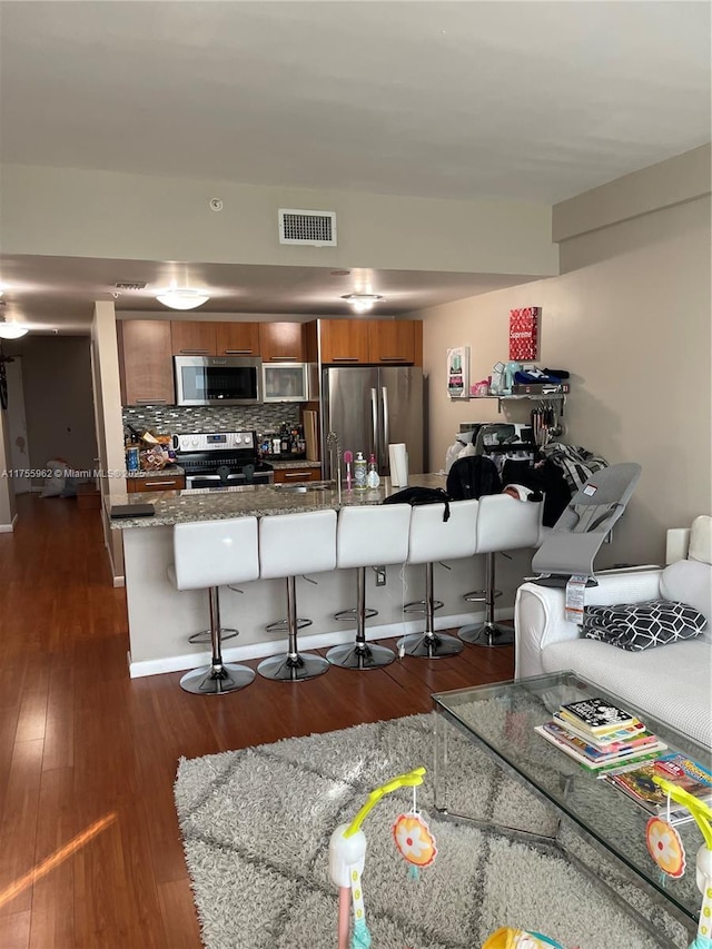 kitchen featuring appliances with stainless steel finishes, brown cabinetry, visible vents, and a kitchen breakfast bar