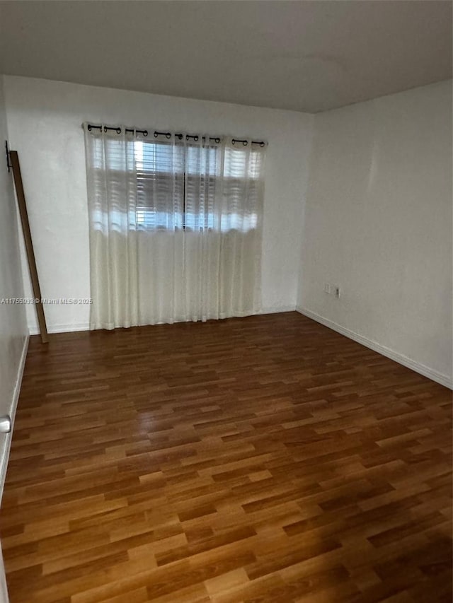 spare room with baseboards and wood finished floors