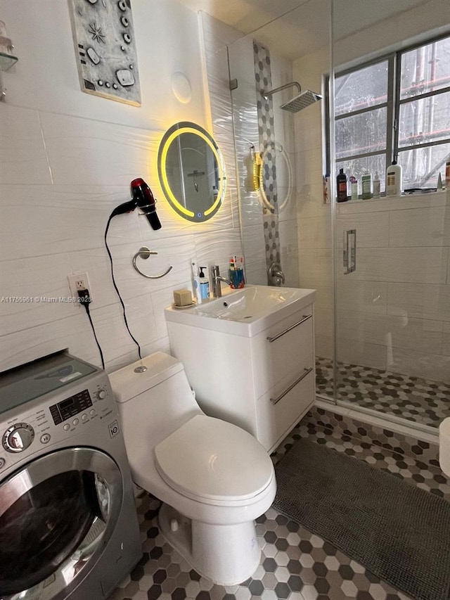 bathroom featuring tile walls, toilet, a shower stall, vanity, and washer / dryer