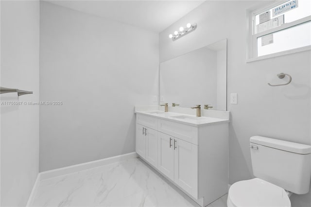 bathroom with toilet, a sink, marble finish floor, and baseboards