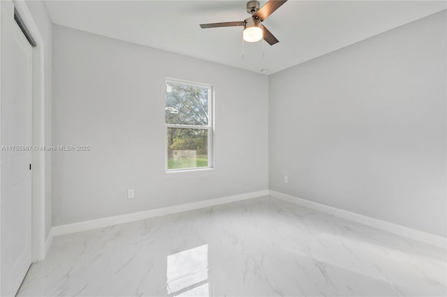 spare room with a ceiling fan, marble finish floor, and baseboards