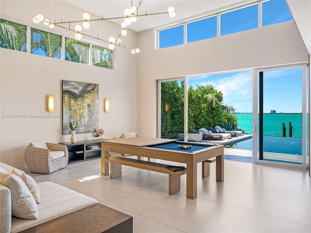 rec room with a water view, a towering ceiling, and a notable chandelier