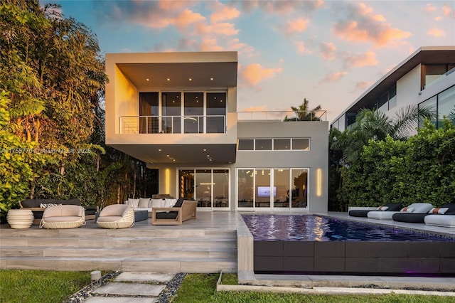 rear view of house with outdoor lounge area, a balcony, and stucco siding