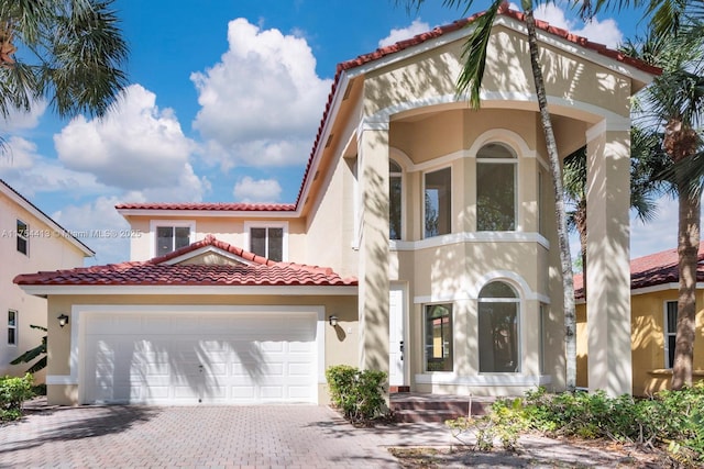 mediterranean / spanish house with decorative driveway, a tiled roof, an attached garage, and stucco siding