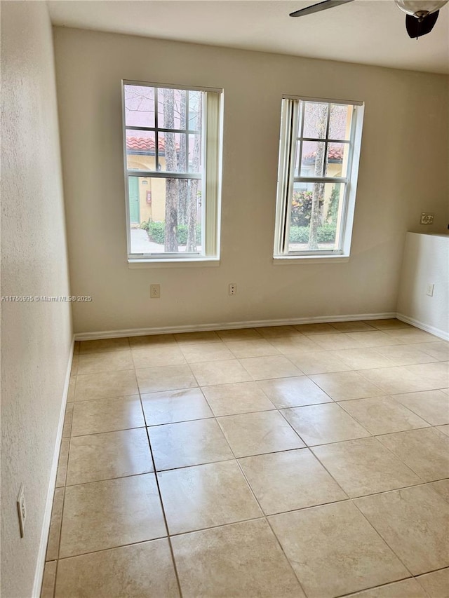 empty room with light tile patterned floors, baseboards, a ceiling fan, and a textured wall