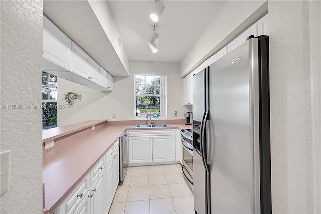 kitchen with light tile patterned floors, stainless steel appliances, light countertops, white cabinets, and a sink