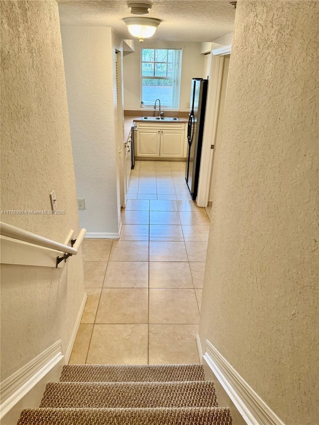 corridor featuring a textured ceiling, a textured wall, light tile patterned floors, and a sink