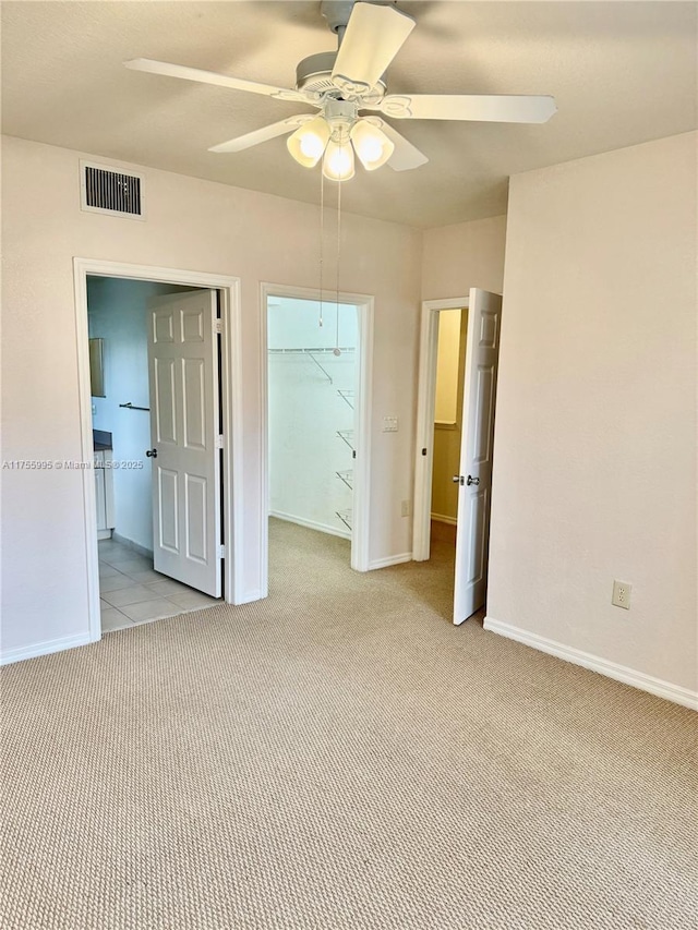 unfurnished bedroom featuring a walk in closet, a closet, visible vents, light carpet, and baseboards