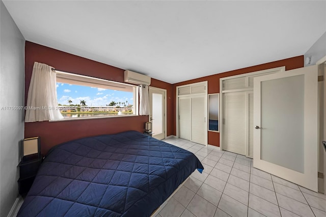 bedroom featuring multiple closets, light tile patterned floors, baseboards, and an AC wall unit