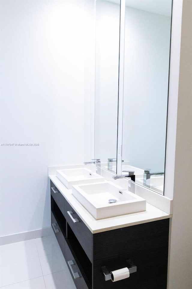 full bath with double vanity, baseboards, a sink, and tile patterned floors