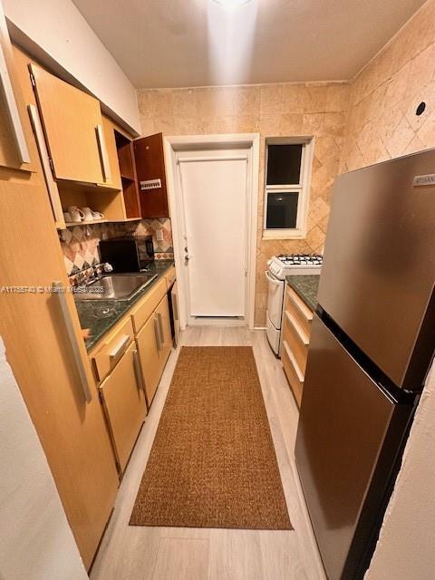 kitchen with white gas range oven, dark countertops, freestanding refrigerator, a sink, and backsplash