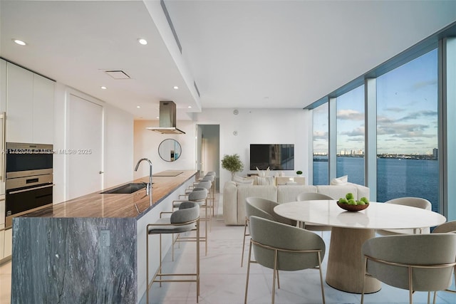 kitchen featuring recessed lighting, a kitchen breakfast bar, island exhaust hood, white cabinets, and a sink