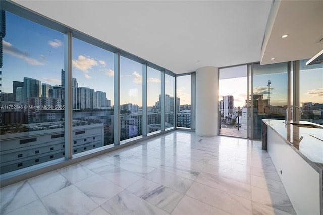 unfurnished room with a city view, a wall of windows, recessed lighting, and a sink
