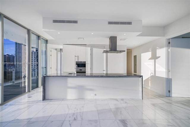 kitchen with visible vents, modern cabinets, white cabinetry, dark stone counters, and island range hood