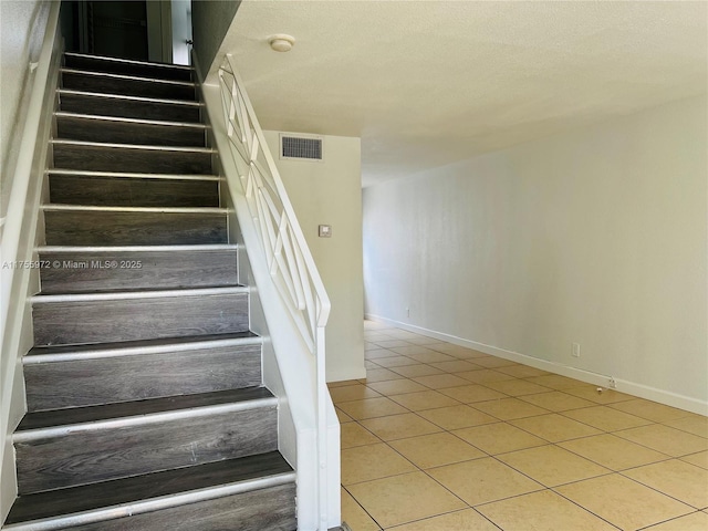 staircase featuring visible vents, a textured ceiling, baseboards, and tile patterned floors