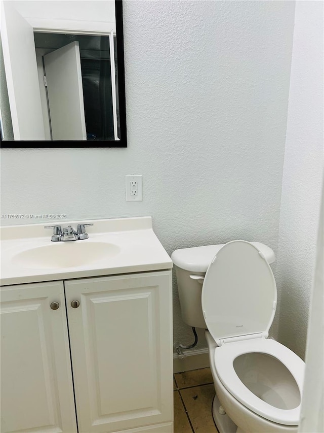 half bath with a textured wall, vanity, toilet, and tile patterned floors