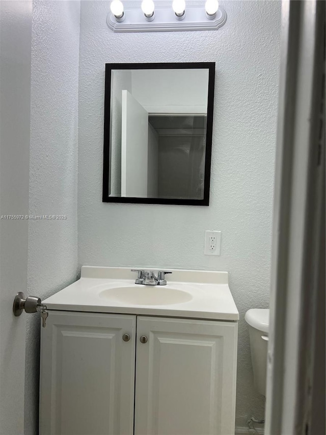 bathroom featuring toilet, a textured wall, and vanity