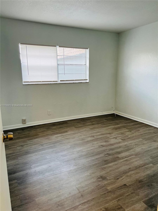 spare room featuring dark wood finished floors, a textured ceiling, and baseboards