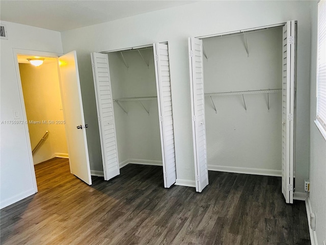 unfurnished bedroom featuring wood finished floors, two closets, visible vents, and baseboards