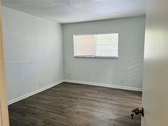 empty room with dark wood-style flooring, a textured ceiling, and baseboards