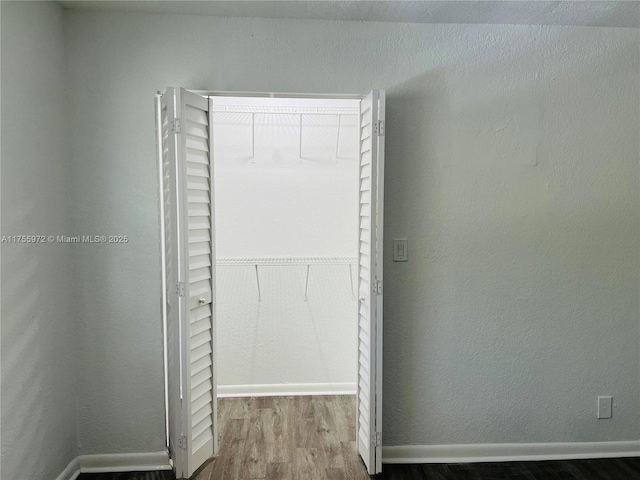 interior space featuring a textured wall, wood finished floors, and baseboards