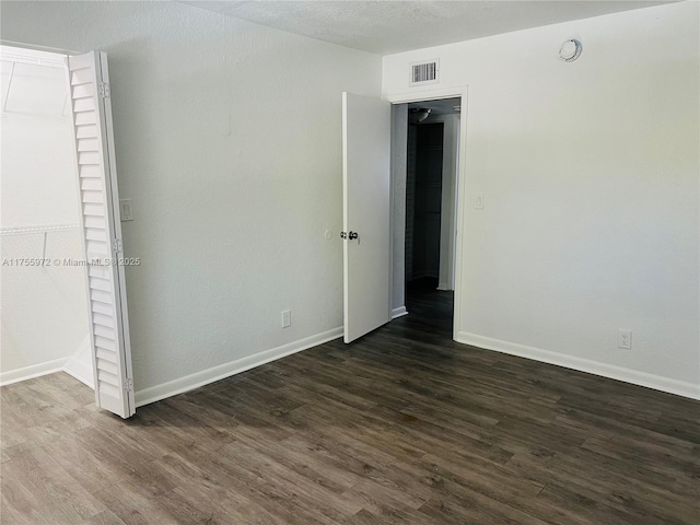 unfurnished bedroom with visible vents, a textured ceiling, baseboards, and dark wood-style flooring